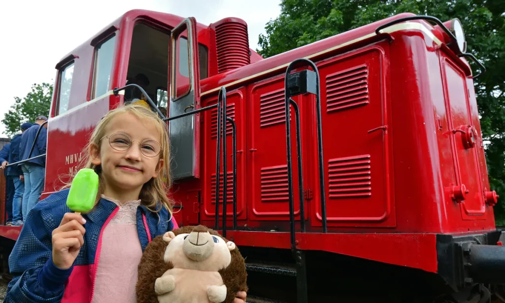 Barn med bamse nyder en is foran et rødt veterantog under Bamsedag ved Mariager-Handest Veteranjernbane.